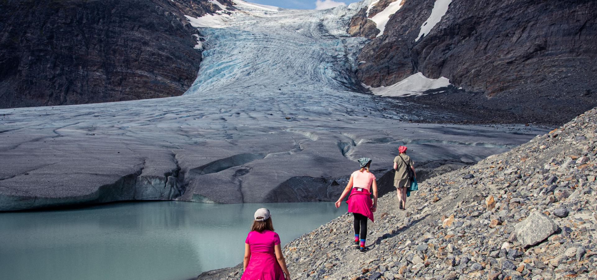 3 persons walking towards the glacier on a rocky ground