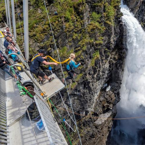 People standing on a walkway bridge over a deep canyon and one person doing a bungee jump
