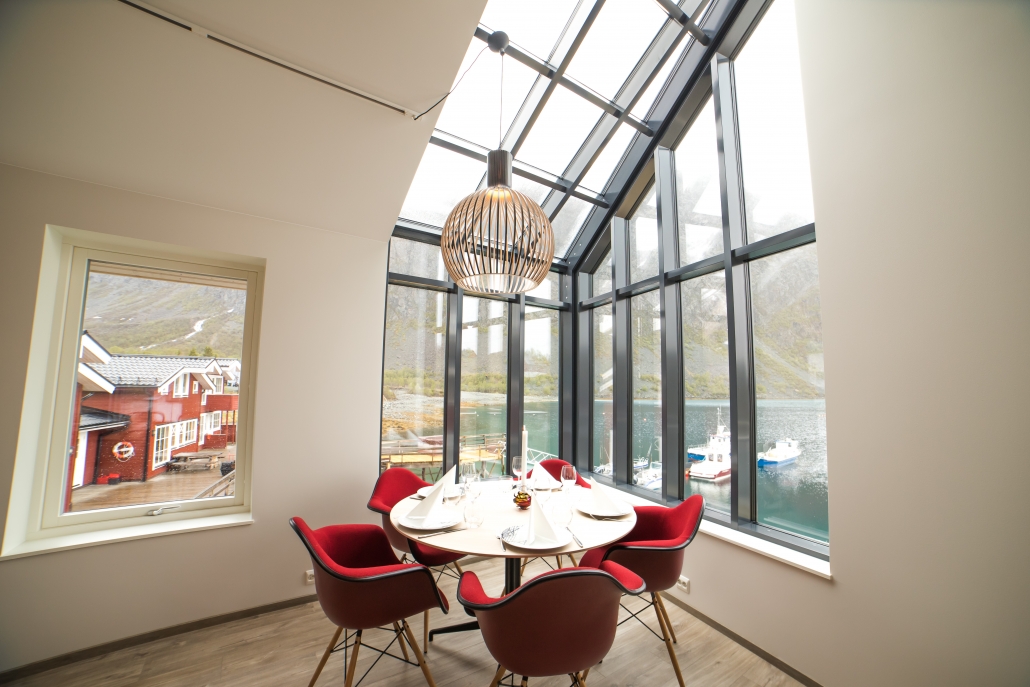 Corner table with red chairs around in front of a panorama window. @koppangenbrygger