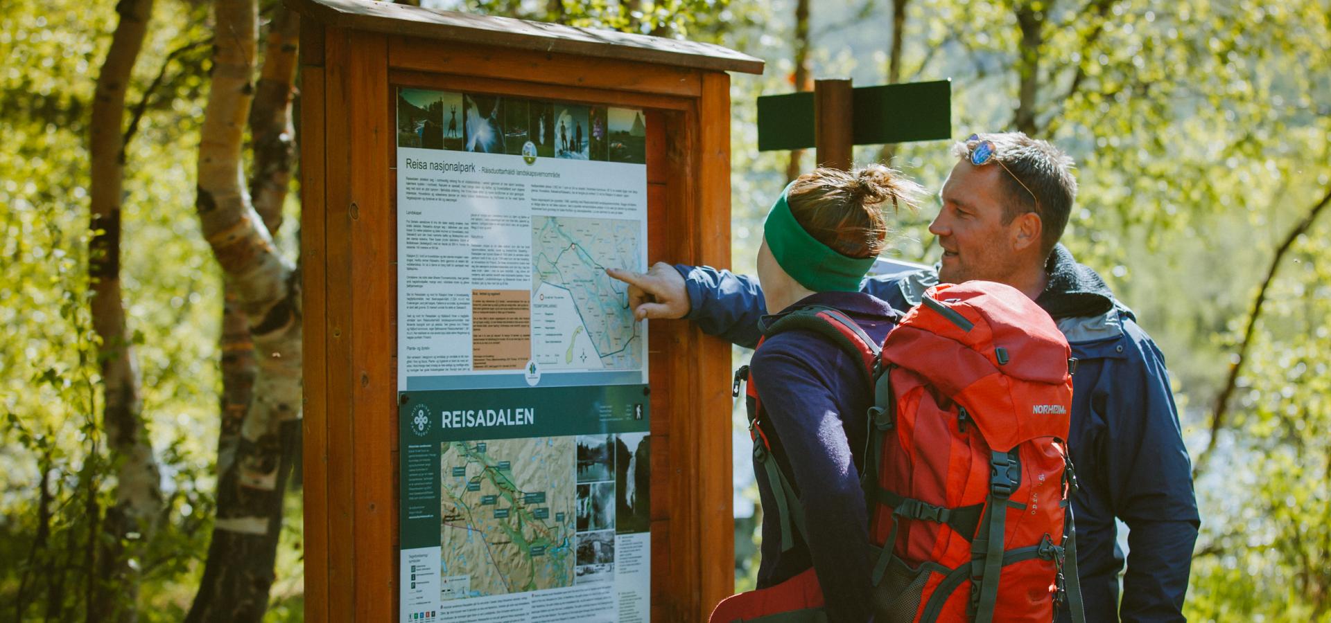 To turkledde personer tar en titt på infotavlen om Reisadalen før turen