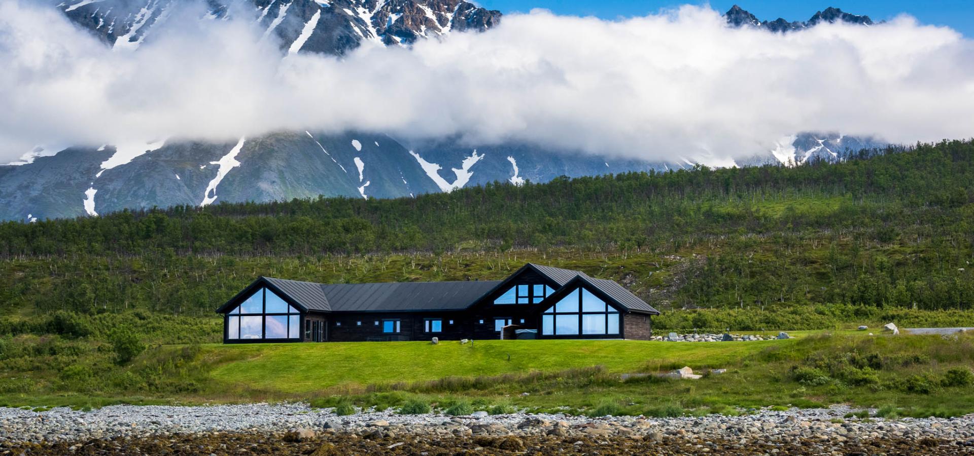 Lyngen Experience Lodge med Lyngsalpene i bakgrunnen og fjorden foran