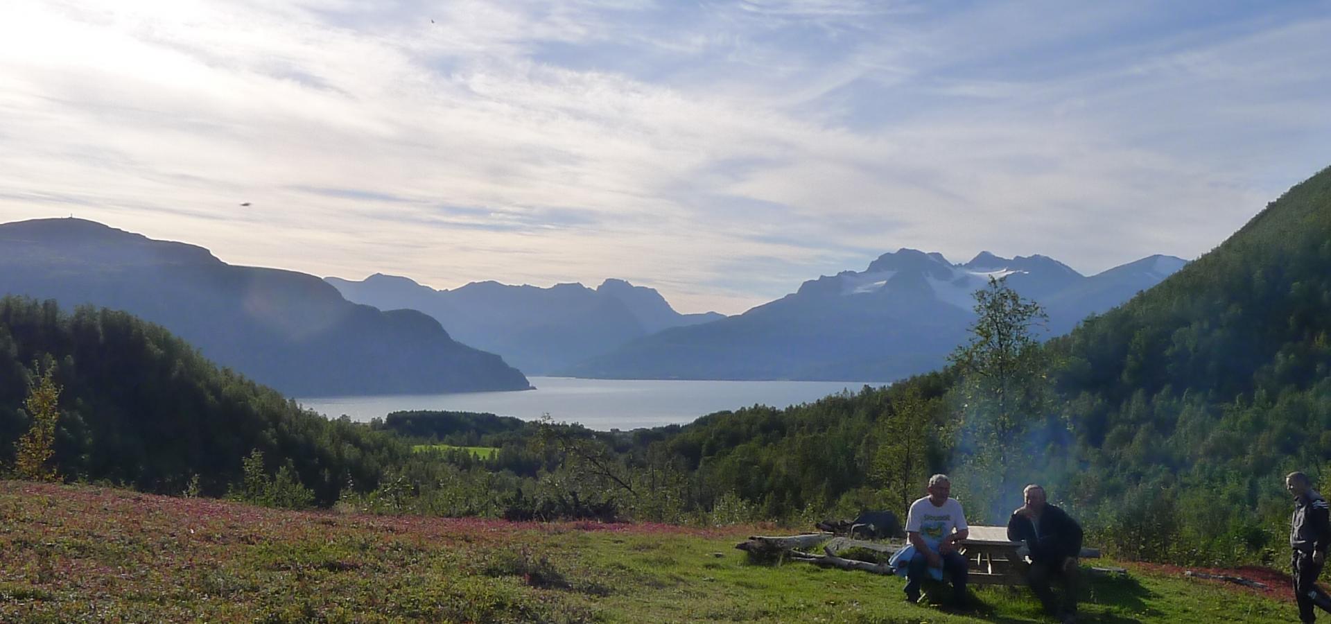 Two persons sitting on a outdoor table, in the background the fjord and the mountains