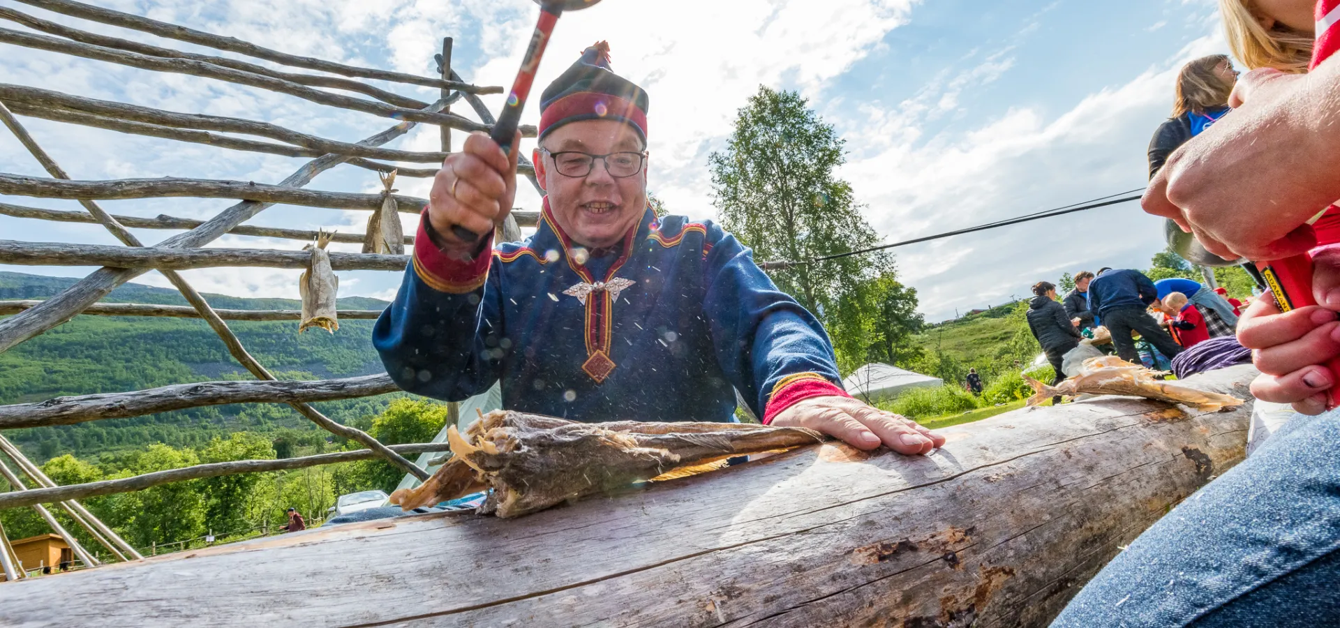 Hammering dried fish, wearing a sami suit