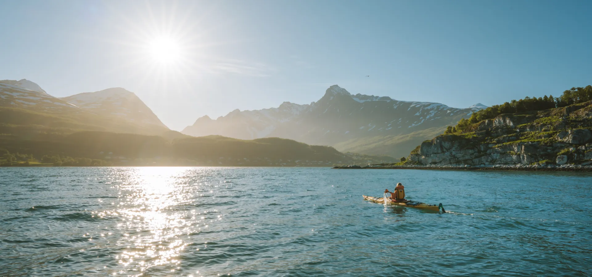 Person in a kayak in the evening sun, paddling towards Lyngseidet