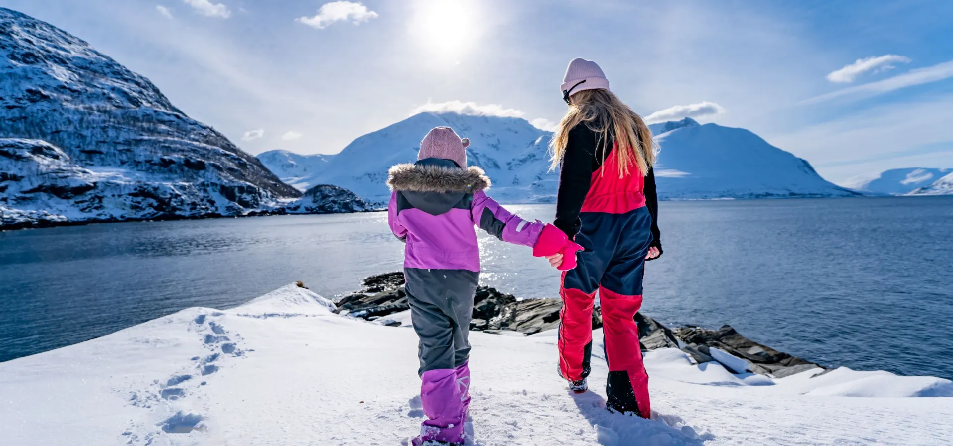 Dame og barn går ut mot havet, bakken er dekt av snø, å solen skinner.