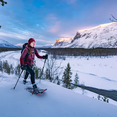 Woman snowshoeing in the winter. She wears a pink jacket and headband.