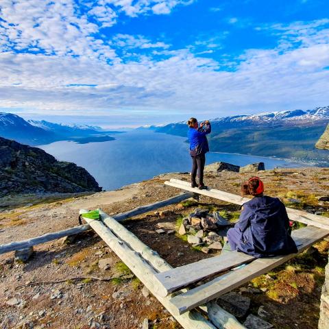 Two persons sitting/standing around a fireplace, enjoying the view of the Lyngenfjord and the LyngenAlps from above