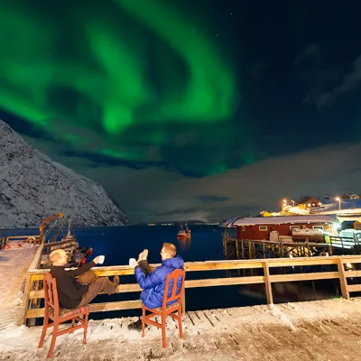 To personer som sitter på kaia en vinterskveld og ser på nordlyset
