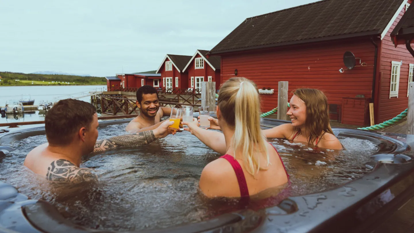 4 persons in a outdoor jacuzzi, red sea side cabins in the background