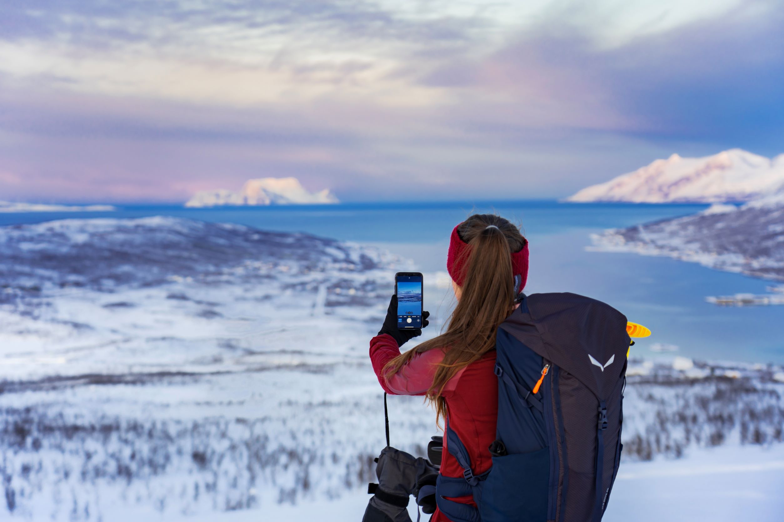 Står med mobilen en kald vinterdag og tar bilde utover et snødekt fjordlandskap